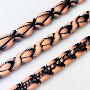 May include: Three copper magnetic bracelets with different link styles. The top bracelet has oval links, the middle bracelet has a woven design, and the bottom bracelet has a mesh design.