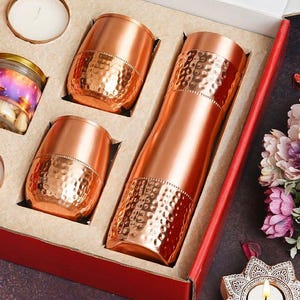 以下が含まれることがあります： 銅色のギフトセット。ハンマー加工が施された水筒とタンブラー2個が含まれています。赤い箱に入っており、キャンドルと瓶も添えられています。アイテムは光沢のある金属仕上げです。