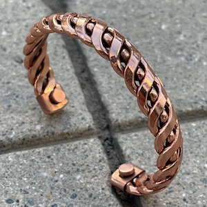 May include: A copper magnetic bracelet with a braided design. The bracelet is open and has a magnetic clasp.