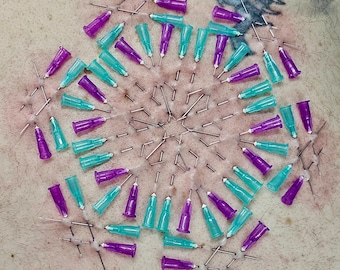 May include: Close-up of a circular arrangement of medical needles and purple and teal syringe tips. The needles are inserted into the skin, and the syringe tips are arranged in a radial pattern. The skin has visible stitches.