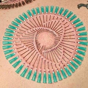 Peut inclure: Gros plan sur le dos d'une personne avec un motif circulaire de 50 petites aiguilles bleu turquoise insérées dans la peau. Les aiguilles sont disposées en spirale, les pointes vers l'extérieur.