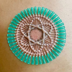 Może przedstawiać: Zbliżenie na skórę osoby z okrągłym wzorem włożonych w skórę igieł w kolorze turkusowym.