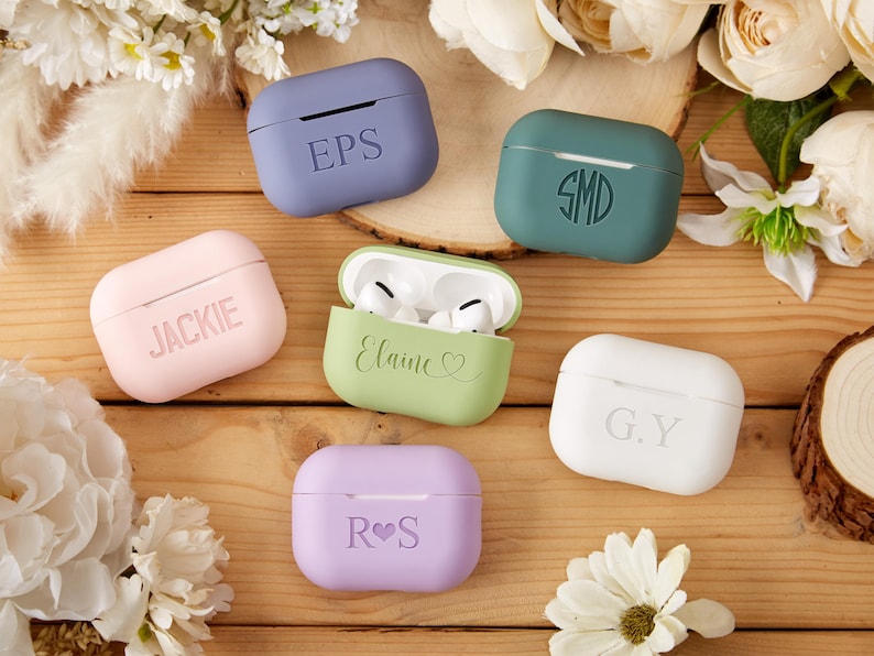 May include: Six personalized AirPod cases in various colors, including pink, green, purple, white, and blue. The cases feature different names and initials, such as "Jackie", "Elaine", "R.S.", "G.Y.", "S.M.D.", and "EPS".