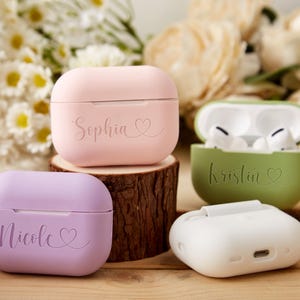 May include: Four personalized AirPod cases in pink, purple, green, and white with the names Sophia, Kristin, Nicole, and a heart symbol.