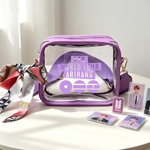 May include: A clear, purple-trimmed crossbody bag with a shoulder strap and a patterned scarf. The bag features the text "BTS WORLD TOUR ARIRANG" and includes several photo cards and a logo. The bag is on a white surface.