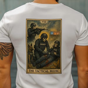 May include: White t-shirt featuring a tarot card design with a tactical medic theme. The artwork depicts skeletal figures in police and paramedic uniforms, with the text "THE TACTICAL MEDIC" at the bottom. The design includes a dog and the Roman numeral VIII.
