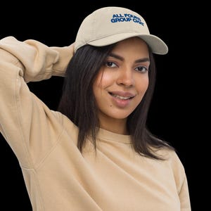 May include: A person wearing a beige sweatshirt and a beige baseball cap with the text "ALL FOURS GROUP CHAT" embroidered in blue.