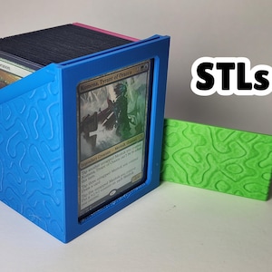 May include: A blue card storage box with a textured design, holding a deck of cards. A green card holder is next to the box. The text "STLs" is in the upper right corner.