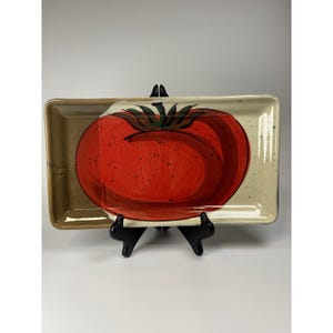 May include: Rectangular ceramic serving platter with a hand-painted red tomato design. The tomato has green leaves and is centered on a cream-colored background with brown speckles. The platter has a brown border.