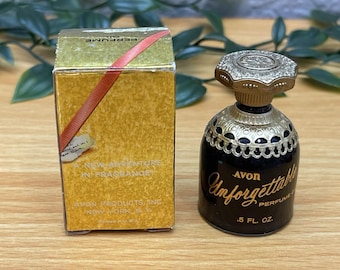May include: A small black Avon Unforgettable perfume oil bottle with a gold-toned ornate cap and collar, labeled .5 fl. oz. Beside it stands a rectangular gold box with a red diagonal stripe, marked A New Adventure In Fragrance.