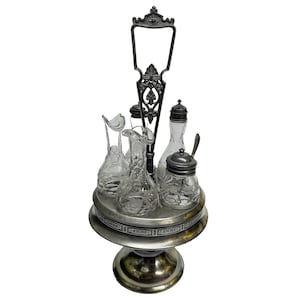 May include: An antique silver-plated condiment set with four glass bottles and jars. The set includes a handle and sits on a round base. The glass bottles and jars have a decorative design.