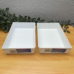 May include: Two rectangular white plastic drawer organizers with open tops. Each tray features a blue product label on the front side with a barcode and the text Rubbermaid Drawer Organizer 9 in x 6 in x 2 in / 22.9 cm x 15.2 cm x 5.1 cm.