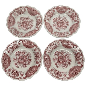 May include: Four white ceramic plates with a red floral pattern and scalloped edges. The plates feature a central floral design and decorative border elements. A classic design for serving food.