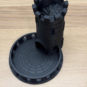 May include: A black 3D-printed dice tower in the shape of a castle tower. The tower has a spiral staircase inside and a circular base with a patterned design. The tower is designed for tabletop gaming.