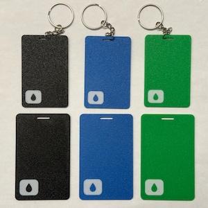 Peut inclure: Six porte-clés avec des étiquettes rectangulaires de différentes couleurs. Chaque étiquette a un anneau argenté et une icône de goutte d'eau blanche. Les couleurs sont noir, bleu, vert, noir, bleu et vert.