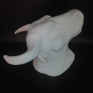 Puede incluir: Una escultura blanca de la cabeza de un toro con cuernos curvados. La obra de arte se encuentra sobre un fondo negro, resaltando los detalles de la cara y los cuernos del toro. Una pieza decorativa.