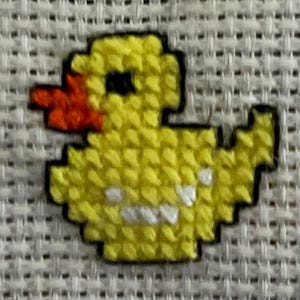 May include: A cross-stitched yellow duck with an orange beak and black eyes. The duck is outlined in black and stitched on a white fabric background. The duck is a pixelated design.