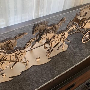 May include: A wooden stagecoach model pulled by a team of horses. The horses are in mid-gallop, and the stagecoach has detailed wheels and seating. The model is made of light-colored wood with dark etched details.