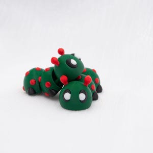 May include: Three green and red ladybug figurines with white eyes. The ladybugs are stacked on top of each other.