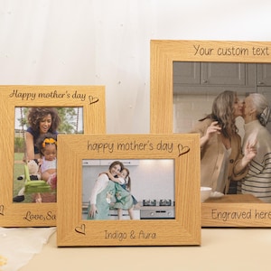 Peut inclure: Trois cadres photo en bois clair avec des photos. Les cadres portent les inscriptions "Happy mother's day" et "Your custom text". Des cœurs sont également gravés sur les cadres.