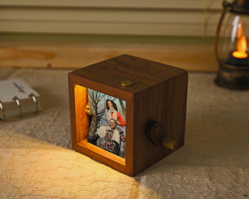 May include: A wooden music box in a cube shape, with a photo of two people visible. The box has a crank on the side and the words "together forever" engraved on top. A small lamp is in the background.