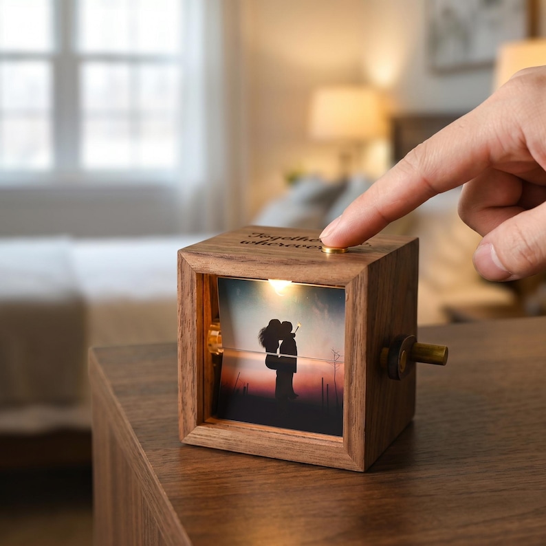 May include: A wooden music box featuring a photograph of a couple kissing. The box has a small light and a crank. The text "Together wherever" is engraved on the top. A finger is pressing a gold button on the top of the box.