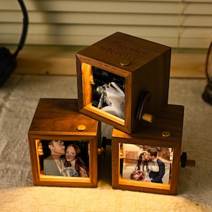 May include: Three wooden photo cubes displaying illuminated pictures of couples. The cubes are engraved with the words "Forever Love" and "Together wherever". Each cube has a small crank and a gold-coloured button.