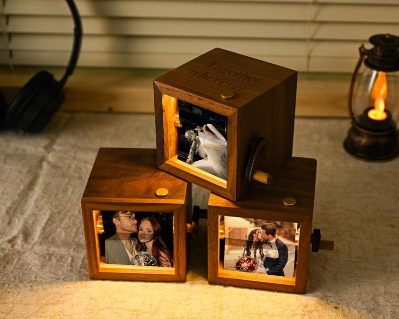 May include: Three wooden photo cubes displaying illuminated pictures of couples. The cubes are engraved with the words "Forever Love" and "Together wherever". Each cube has a small crank and a gold-coloured button.