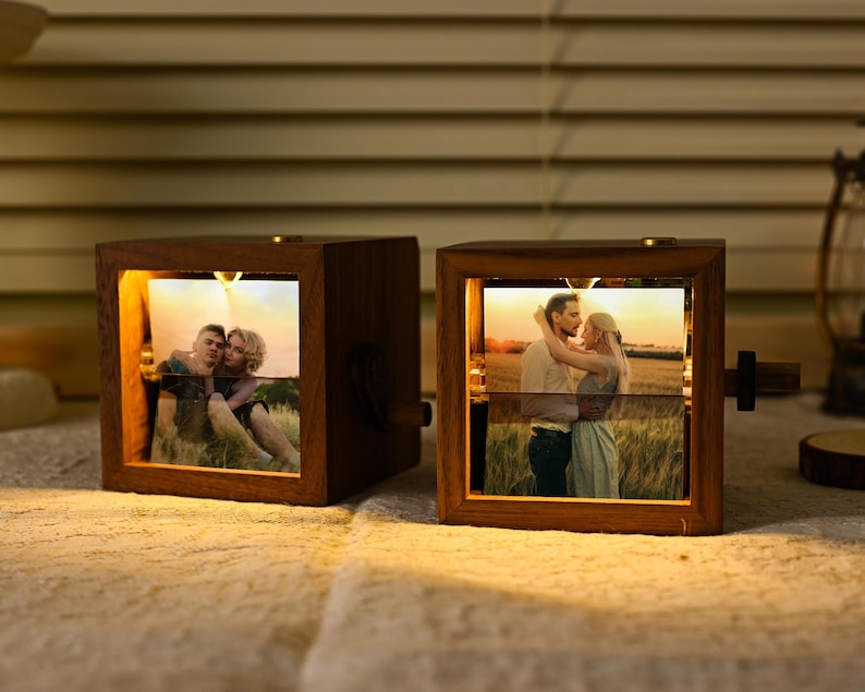 May include: Two wooden photo cubes with illuminated pictures of couples. The cubes have a warm glow, and a small knob on the side. The photos are displayed horizontally, and the wood has a rich, dark tone. The cubes are lit.