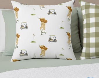 Könnte beinhalten: Quadratisches weißes Kissen mit Golfmotiv. Das Design zeigt ein sich wiederholendes Muster eines Teddybär-Golfers, Golfwagen, Golffahnen und den Namen "Tom" in Schreibschrift. Das Kissen liegt auf einem Bett mit anderen Kissen.