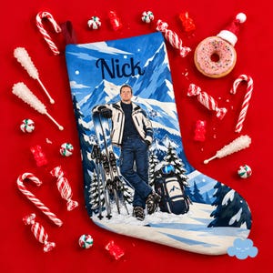 Op de afbeelding: Een blauwe kerstkous met een bedrukte illustratie van een persoon in skikleding die met ski's in een besneeuwd berglandschap staat. De naam Nick staat bovenaan in donkerblauw handschrift gedrukt. Omringd door verschillende soorten snoep.