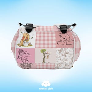 May include: Pink and white checkered diaper bag with Winnie the Pooh and Piglet characters. The bag has a black strap and a white zipper.