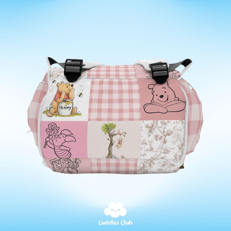 May include: Pink and white checkered diaper bag with Winnie the Pooh and Piglet characters. The bag has a black strap and a white zipper.