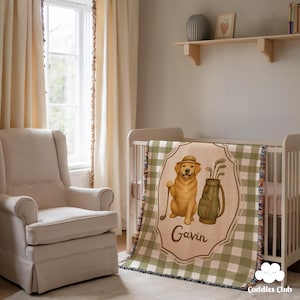 Puede incluir: Una manta para bebé con un estampado de cuadros verdes y blancos. La manta presenta una ilustración de dibujos animados de un golden retriever con sombrero y un palo de golf. El nombre "Gavin" está impreso en la manta.
