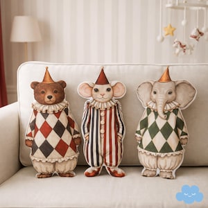 Könnte beinhalten: Drei Zirkustierkissen: ein Bär, eine Maus und ein Elefant. Jedes trägt ein Harlekin-Outfit mit Rüschenkragen und spitzem Hut. Das Outfit des Bären hat rot-schwarze und weiße Rauten. Das Outfit der Maus ist gestreift. Das Outfit des Elefanten hat grüne und weiße Rauten.