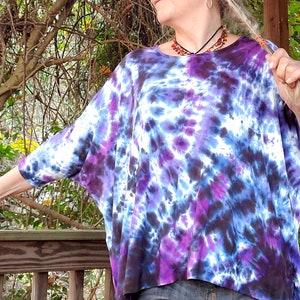 May include: A purple, blue, and white tie-dye shirt with a loose, flowing fit. The shirt has a round neckline and long sleeves.