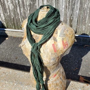 May include: A dark green scarf made of a soft, drapey fabric. The scarf is tied in a loose knot around the neck of a mannequin.