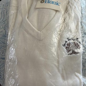 May include: Off-white V-neck sweater, still in its original packaging. The sweater has a tag with the brand name "Etonic" and the size XL. The left side of the sweater has an embroidered tree design with the words "Apple Valley Resort".