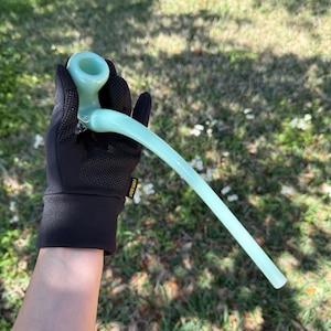 May include: A light blue glass pipe with a long, curved stem. The pipe is being held by a gloved hand.