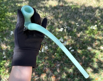 May include: A light blue glass pipe with a long, curved stem. The pipe is being held by a gloved hand.
