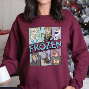 Puede incluir: Sudadera granate con un gr&aacute;fico colorido de personajes de la pel&iacute;cula "Frozen". El dise&ntilde;o incluye a Elsa, Anna, Olaf, Kristoff, Sven y un personaje con un sombrero verde. La palabra "FROZEN" est&aacute; impresa en letras azules.