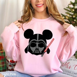 May include: Light pink sweatshirt featuring a black and gray Darth Vader design with Mickey Mouse ears and a red lightsaber. The text "Light Pink" is visible at the bottom left of the image. The sweatshirt is a crew neck style.