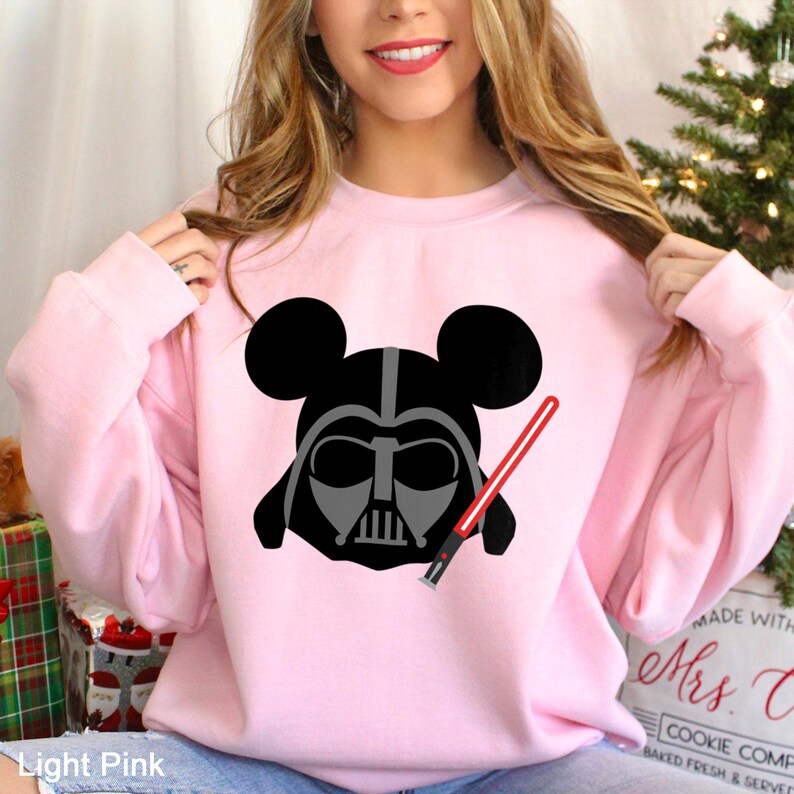 May include: Light pink sweatshirt featuring a black and gray Darth Vader design with Mickey Mouse ears and a red lightsaber. The text "Light Pink" is visible at the bottom left of the image. The sweatshirt is a crew neck style.