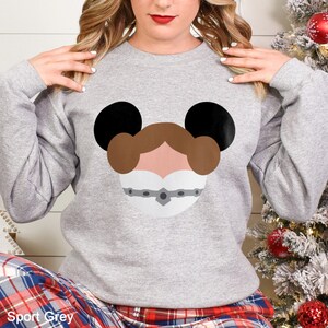 May include: Sport Grey sweatshirt featuring a graphic design of a character's face with black mouse ears. The character's face is brown, white, and gray. The sweatshirt is a long-sleeved crew neck. The text "Sport Grey" is at the bottom.