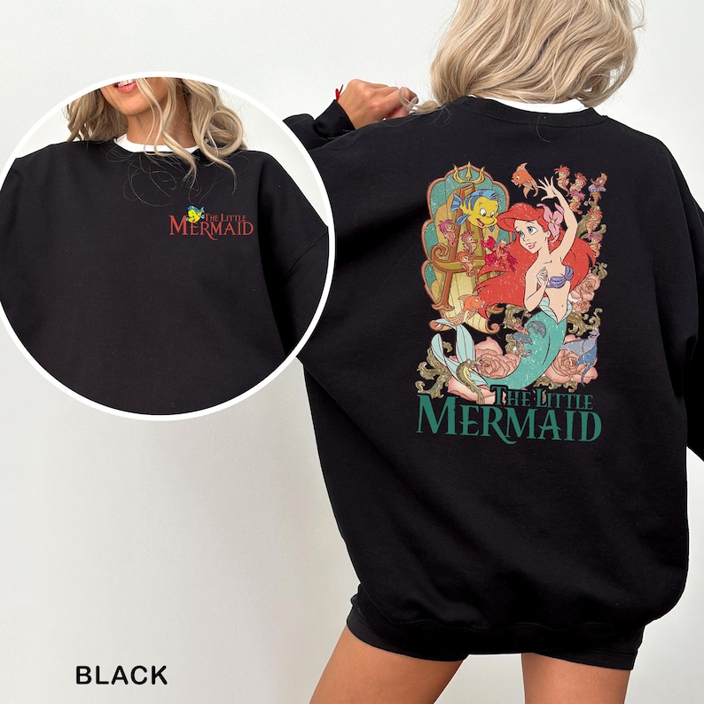 以下が含まれることがあります： 背中にリトルマーメイドのアリエルのカラフルなグラフィックが描かれた黒いスウェットシャツ。左胸には「The Little Mermaid」の文字が入った小さなロゴがあります。スウェットシャツは白い襟が付いています。