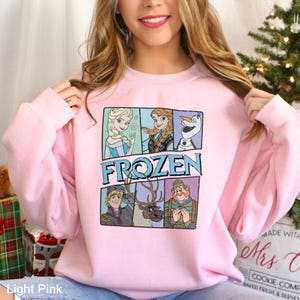 Puede incluir: Sudadera rosa claro con la palabra "FROZEN" e im&aacute;genes de personajes de la pel&iacute;cula animada. El dise&ntilde;o incluye a Elsa, Anna, Olaf, Kristoff, Sven y el duque de Weselton. La sudadera es de cuello redondo.