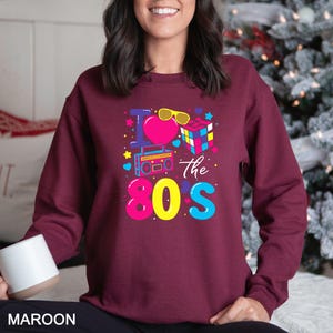 a woman wearing a maroon sweatshirt with the words the 80's printed on it