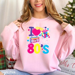 a woman wearing a pink sweatshirt that says i love the 80's