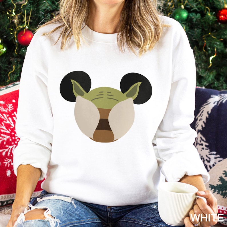 May include: White sweatshirt featuring a cartoon design of a green character with large black ears. The character's face is light green with tan and brown accents. The word "WHITE" is visible on the bottom right of the image.