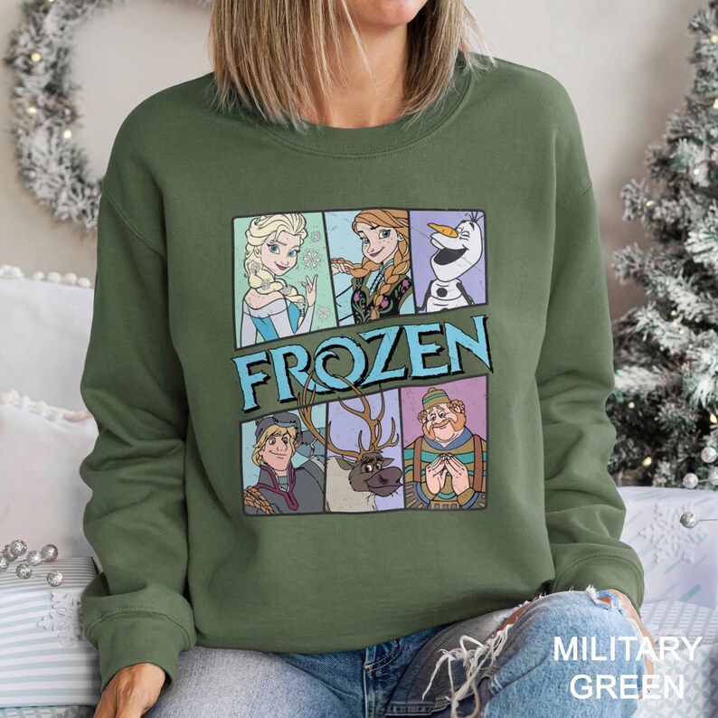 Puede incluir: Sudadera verde militar con un gr&aacute;fico de personajes de la pel&iacute;cula "Frozen". El dise&ntilde;o incluye a Elsa, Anna, Olaf, Kristoff, Sven y un personaje con un su&eacute;ter a rayas. La palabra "FROZEN" est&aacute; impresa en azul en el centro.
